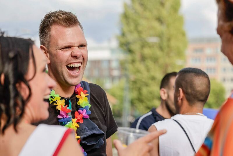 Das Bild zeigt eine lachende Person im Gespräch mit mehreren Gegenüber.