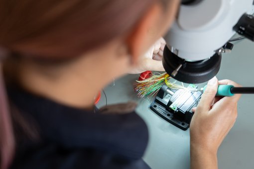 Foto mit Blick über die Schulter einer Frau, die unter dem Mikroskop die Platine einer Ultraschallsonde repariert.