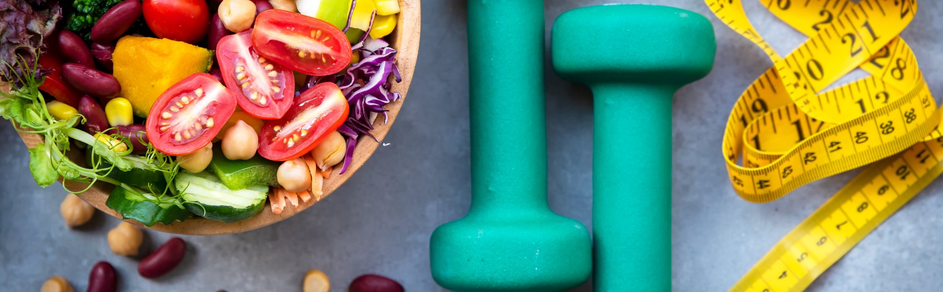 Symbolbild Ernährungstherapie und Ernährungsberatung am Sana Klinikum Borna: Auf dem Bild sind von links nach rechts zu sehen eine Schüssel mit gemischten Gemüse (wie z. B. Tomaten, Bohnen, Mais, Salatblättern etc.), zwei türkisfarbenen Hanteln und einem gelben Massband