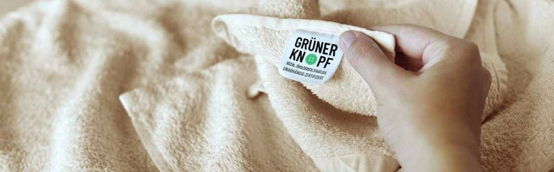 Eine Person zeigt an einem Handtuch das Etikett des Zertifikats "Grüner Knopf".