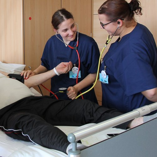 Auszubildende am Patientenbett: lernen mit einem Doppelstethoskop den Blutdruck zu messen