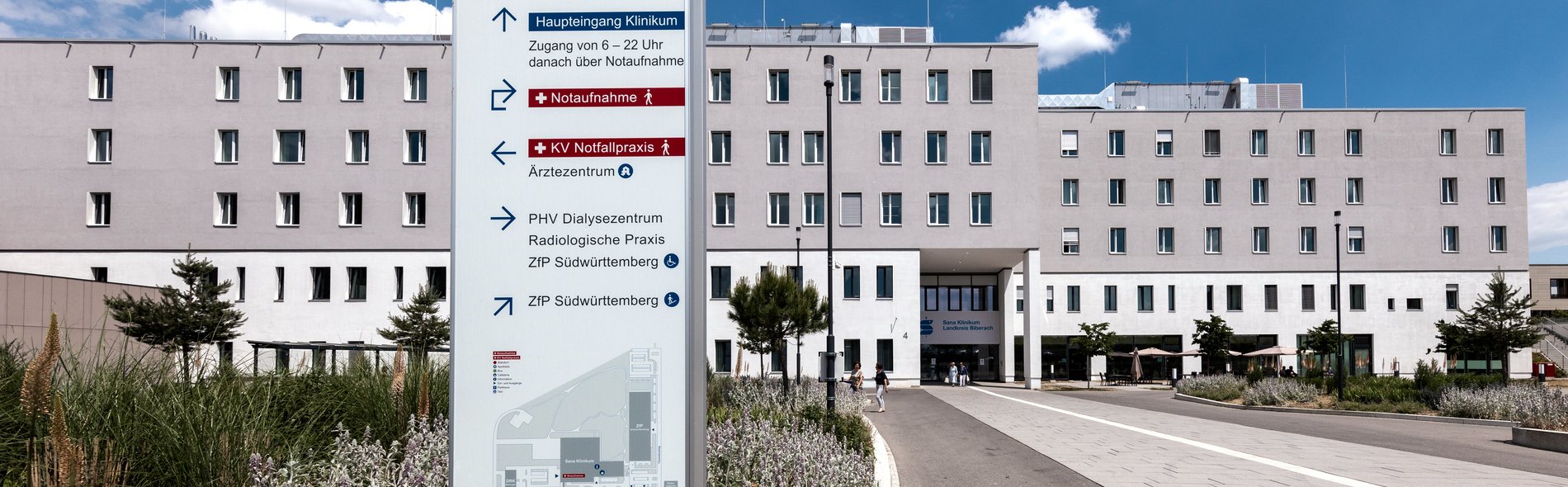 Das Foto zeigt das Zentralgebäude der Sana Kliniken Landkreis Biberach. Ein Hinweisschild zeigt den Weg zum Klinikum und zum Ärztehaus.