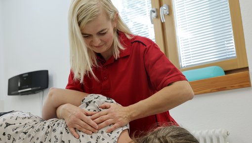 Eine Physiotherapeutin behandelt eine Patientin, die auf einer Liege liegt.