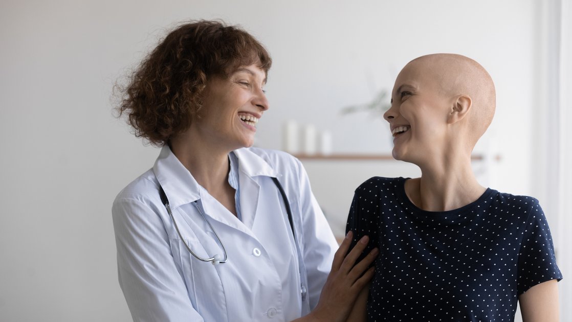 Eine junge Patientin ohne Haare und eine Ärztin lachen zusammen