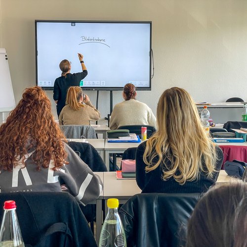 Blick auf die eletronische Tafel, Lehrerin schreibt etwas darauf
