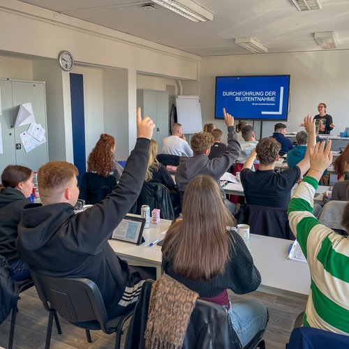 Blick in einen Klassenraum mit Auszubildenden, einige melden sich