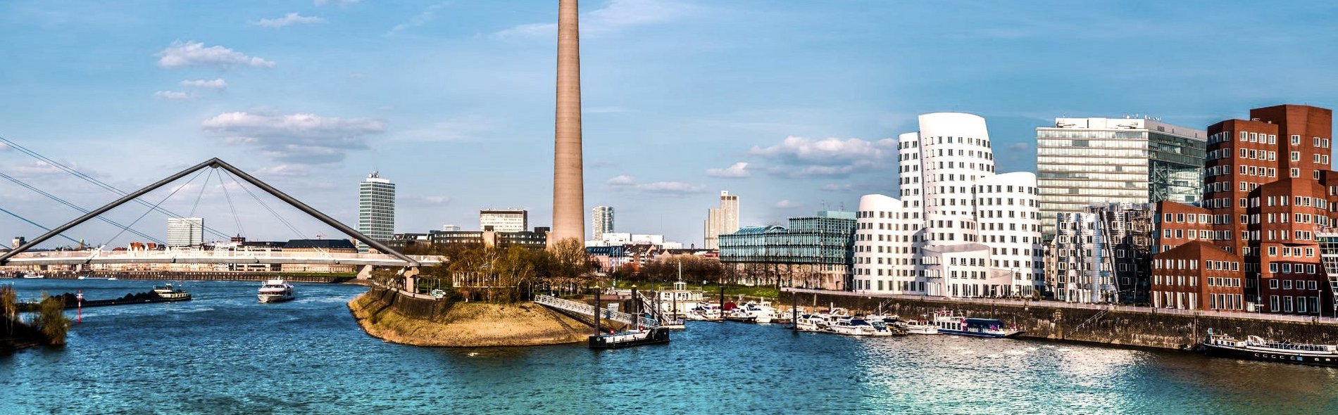 Bild von der Stadt Düsseldorf aus der Wasserperspektive. Mittig sind Brücken und ein Funkturm zu sehen.    